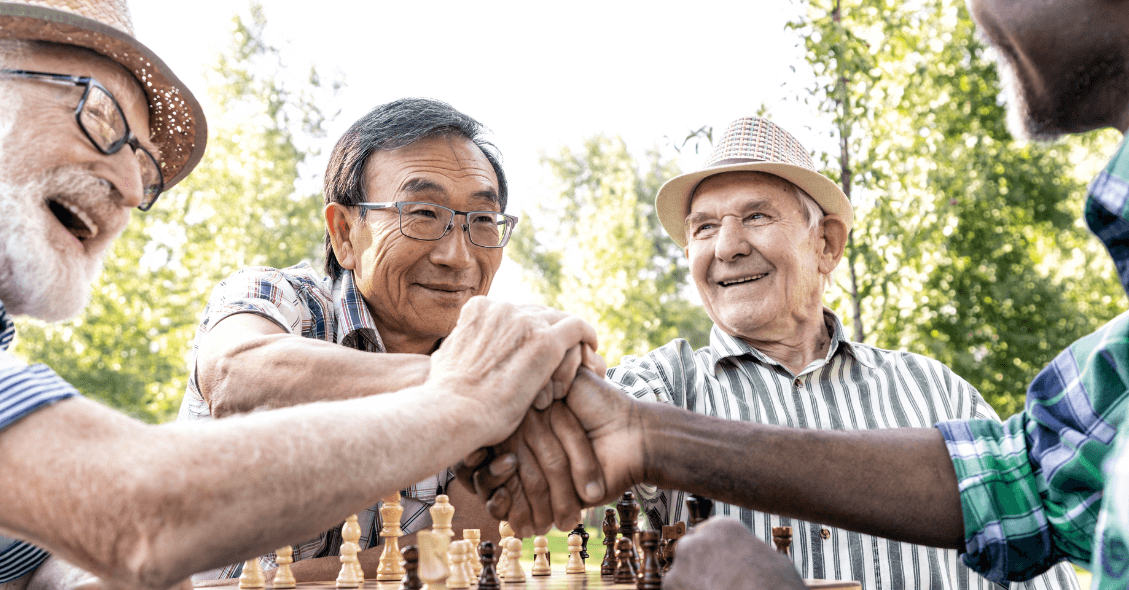 four seniors of diverse backgrounds giving each other a high five during a chess match